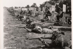 Soldiers firing rifles while wearing gas masks.